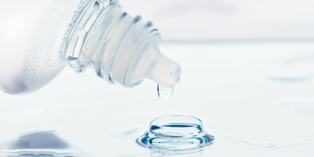 Ein Tropfen treufelt aus einer Plastikflasche in eine Linse